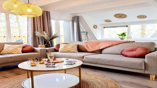 A modern living room with a sofa set, a coffee table, and a large window with curtains. - Renovated Ardennes Chalet with Patio (Durbuy)