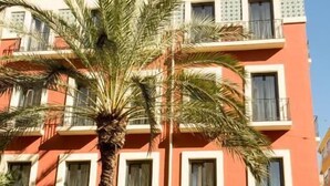Un edificio de varios pisos con balcones, una palmera en primer plano y cielo despejado.