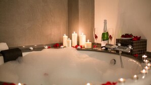 Un jacuzzi rodeado de velas y pétalos de rosa, con una botella de champán y copas a un lado.
