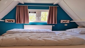 A bedroom with a large bed, two windows with curtains, a radiator, and two wall-mounted pictures of animals. - Comfortable Fenced Chalet in Durbuy (Durbuy)