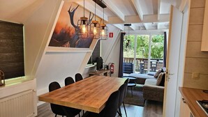 A modern kitchen with a wooden table and black chairs, a painting on the wall, and a view of the outdoor deck. - Comfortable Fenced Chalet in Durbuy (Durbuy)