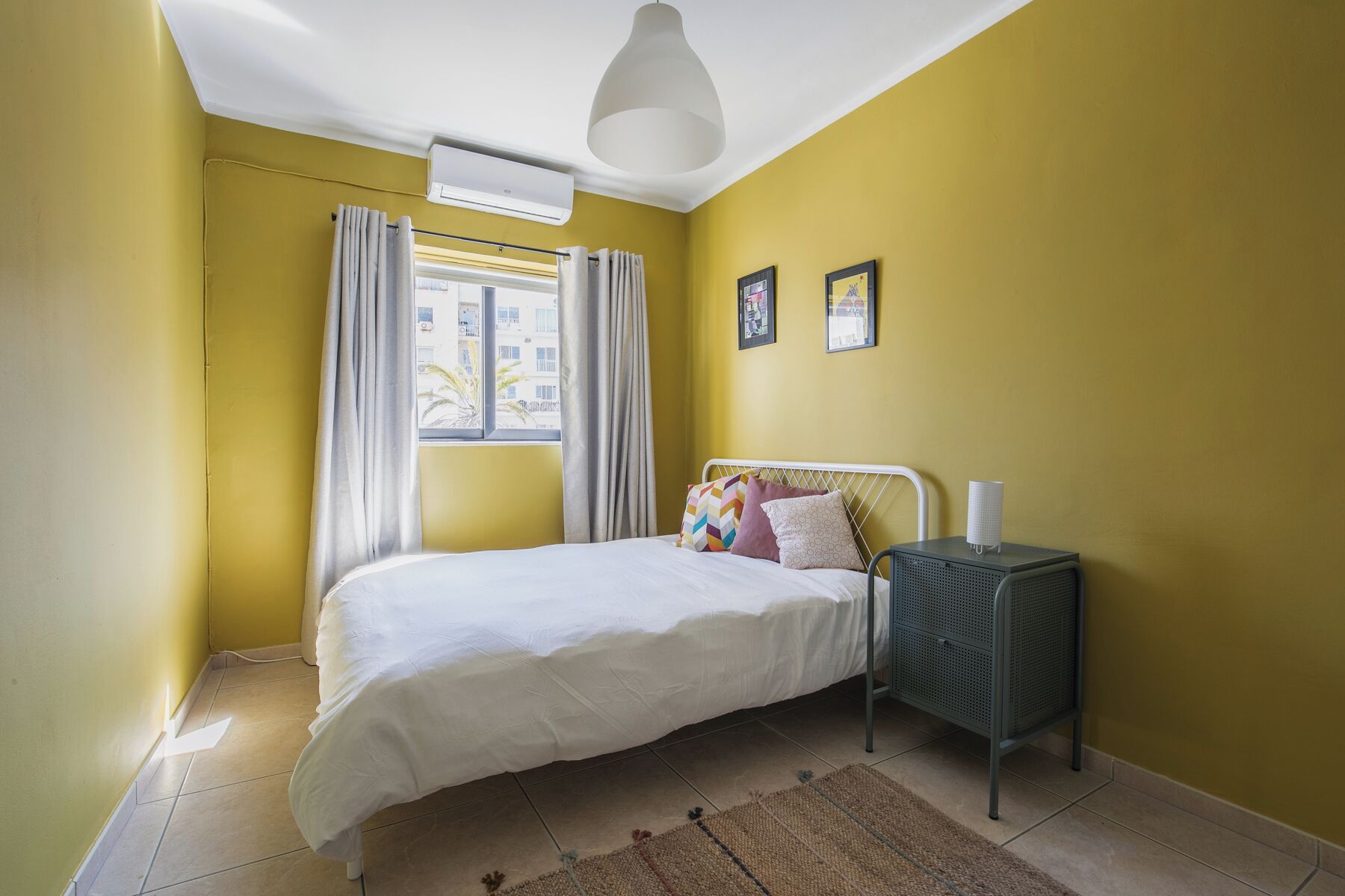 A bedroom with a bed, a nightstand, a lamp, and a window with curtains.