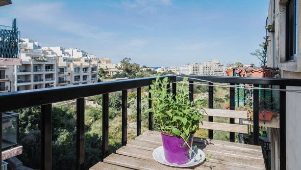 En balkon med et træbord og en lilla potte med grønne planter.