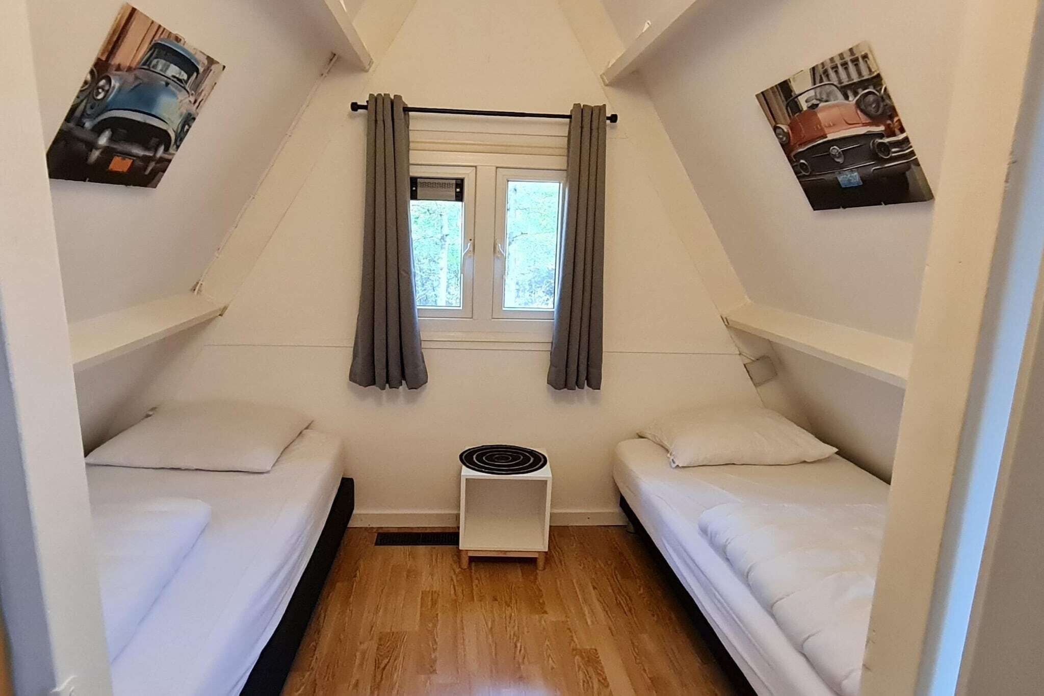 Ein kleiner, dreieckiger Raum mit zwei Betten, einem Fenster mit Vorhängen und einem Wandheizgerät.
