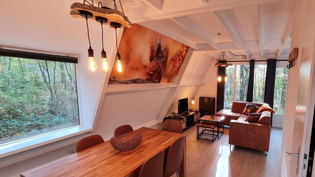 Un intérieur moderne comprenant un coin repas, un canapé et une grande fenêtre donnant sur une forêt.