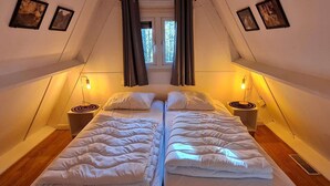 Une chambre avec deux lits, une fenêtre avec des rideaux et des cadres photo accrochés au mur.