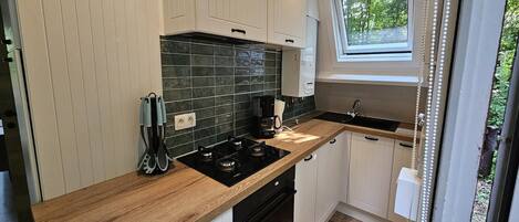 A compact kitchen with white cabinets, a wooden countertop, a built-in stove, and a window providing natural light.