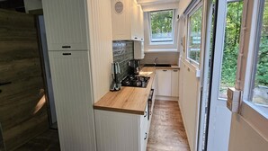 Eine kleine Küche mit weißen Schränken, einer Holz Arbeitsplatte, einem eingebauten Herd und einem Fenster mit Blick ins Grüne.