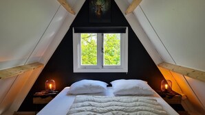Ein Schlafzimmer mit einem Bett, zwei Nachttischen mit Lampen, einem Fenster mit Blick auf Grünflächen und einem Gemälde an der Wand.