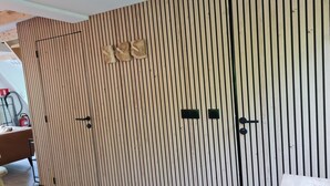 Ein Zimmer mit einer Wand aus Holzlamellen, einem Bett, einem Nachttisch und einem kleinen Schrank.