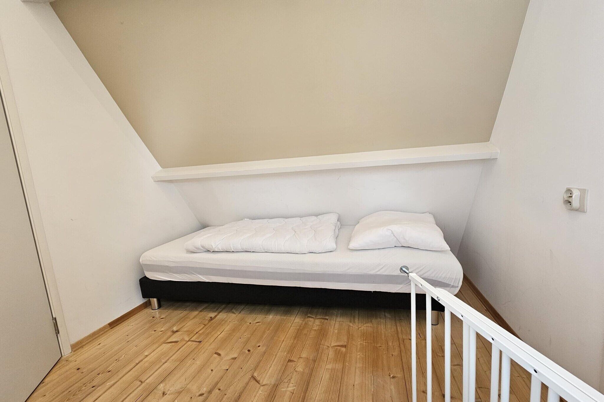 A small, single-bed room with a sloped ceiling and wooden flooring.