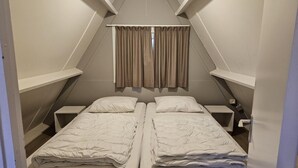 Una piccola stanza triangolare con due letti singoli, un comodino e una finestra con tende.