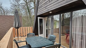 Una terrazza esterna con tavolo e sedie, un pontile in legno e una porta vetrata che dà su un'area coperta.