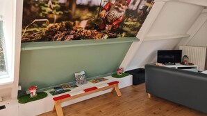 Un salon chaleureux avec un plafond en pente, une bibliothèque, un petit banc et un téléviseur.