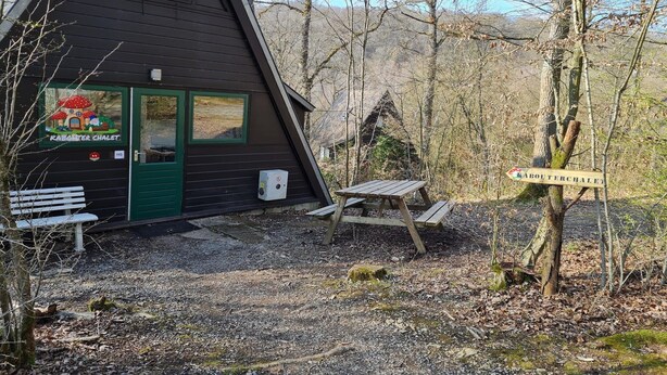 Une cabane avec une porte verte, un banc et une table de pique-nique.