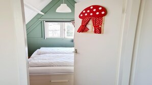 Une chambre à coucher avec un lit, une fenêtre, une porte blanche et un champignon rouge en guise de décoration.