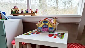 Une petite table pour enfant ornée d’un dessin représentant une maison et des fraises, un tabouret à pois et une étagère avec des figurines.