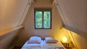 A small, cozy bedroom with a single bed, a bedside table with a lamp, and a window providing a view of greenery outside. - Serene Vacation Chalet in Durbuy (Durbuy)