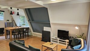 A modern living room with a sofa, a coffee table, a TV, and a fireplace. There is a dining area with a table and chairs.