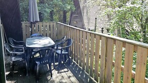 A wooden deck with a table and chairs, surrounded by a wooden fence and trees.