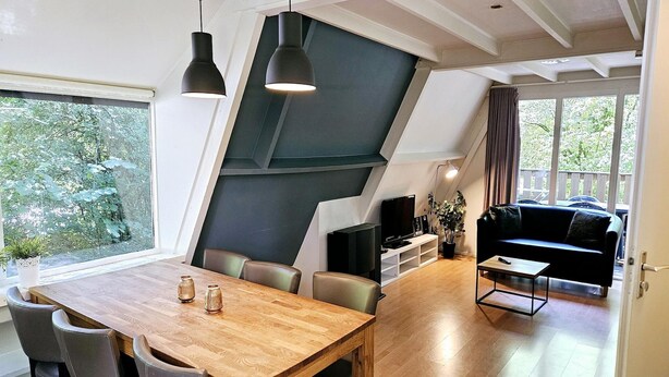 A modern kitchen with a wooden table and chairs, a built-in oven, and a large window overlooking greenery.