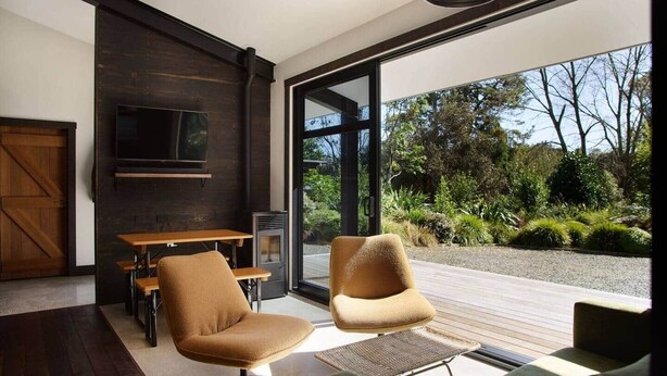Een modern interieur met een houten eettafel, twee fauteuils, een bank en een groot raam met uitzicht op een tuin.