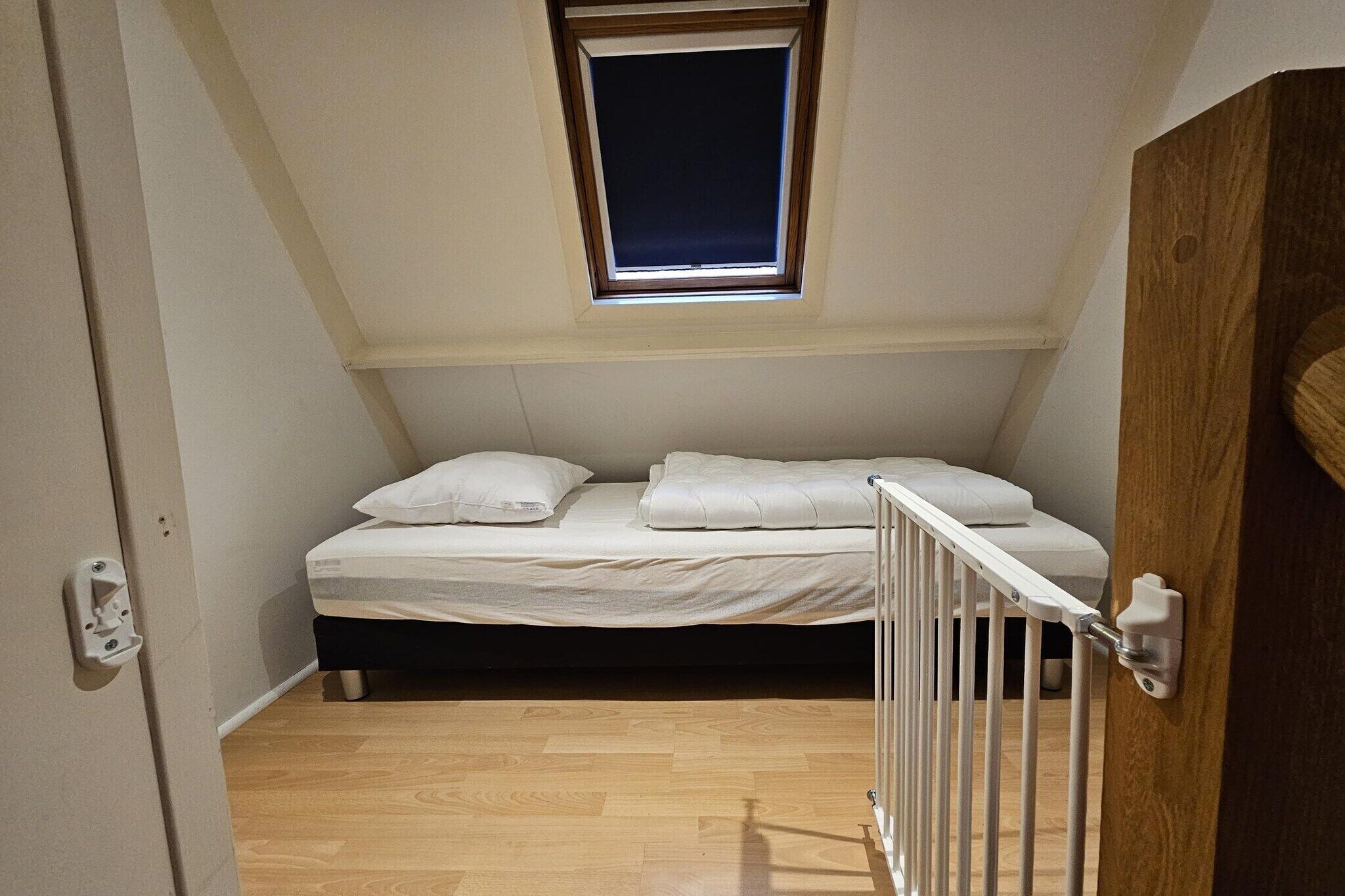 A small, single-bed room with a sloped ceiling and a skylight.