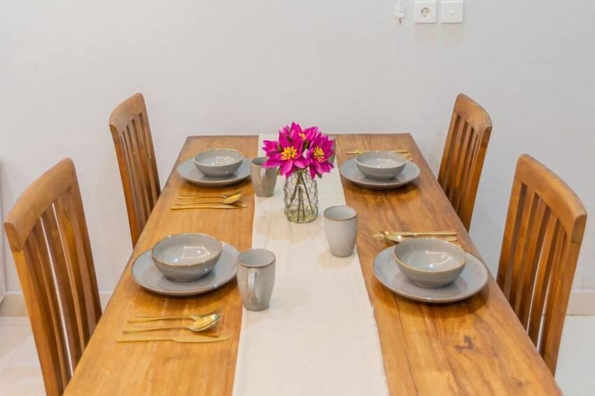 A dining table set with plates, bowls, and cutlery, surrounded by wooden chairs.