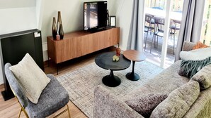 A modern living room with a television on a wooden console, a grey armchair, a round coffee table, and a sofa with a throw blanket. - Tranquil Countryside Stay in Durbuy (Durbuy)