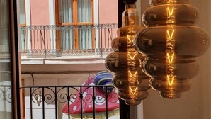 Ein Balkon mit schmiedeeisernem Geländer, ein Fenster mit Holzläden und eine hängende Leuchte mit einem besonderen Design.
