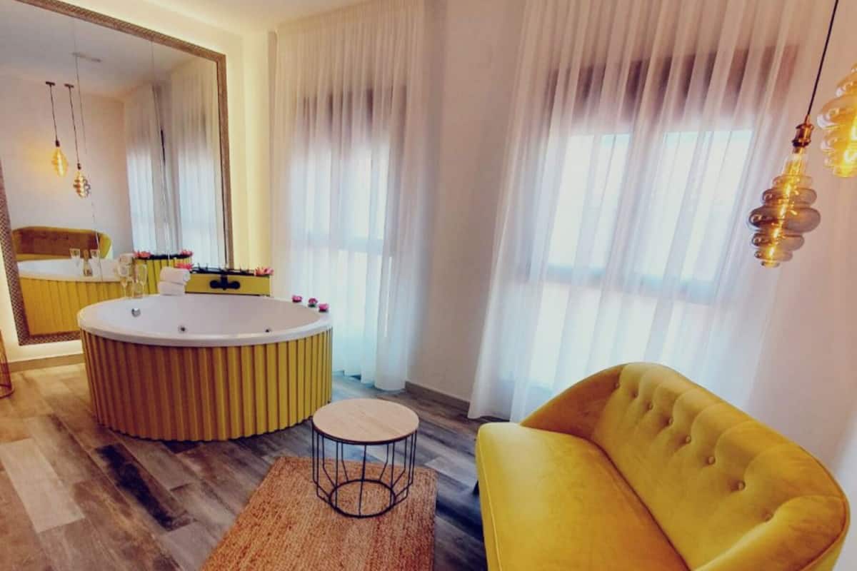 Een moderne woonkamer met een geel sofa, een ronde salontafel en een grote spiegel.