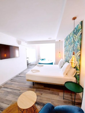 Ein modernes Hotelzimmer mit einem großen Bett, einem flachbildfernseher an der Wand, einem kleinen runden Tisch und einem grünen Stuhl.