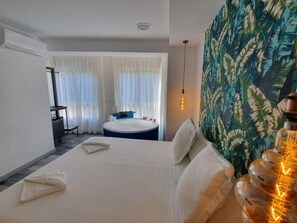 A hotel room with a large bed, a small round table, a bathtub, and a large window with sheer curtains. - Reina Victoria Prado Sastre (Alicante)