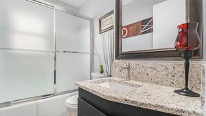 Un baño moderno con encimera de granito, cabina de ducha de vidrio y un espejo grande.