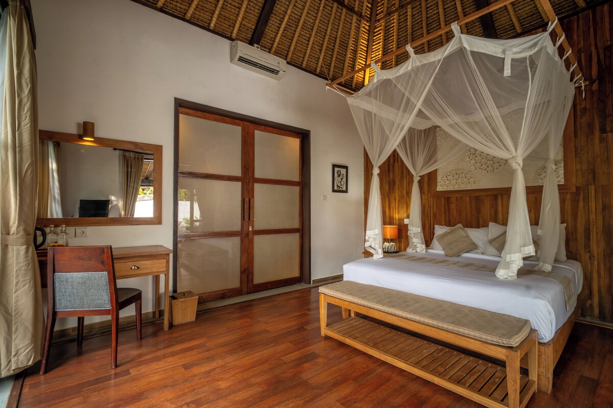 A bedroom with a wooden bed, a desk, a chair, a bench, a large mirror, and a sliding door.