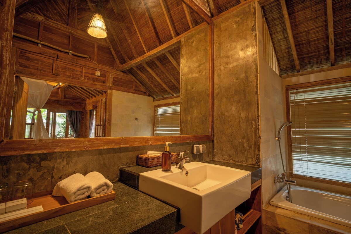 A bathroom with a wooden ceiling, a large mirror, a sink, and a bathtub.