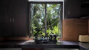Une cuisine équipée d’une cuisinière à gaz, de meubles de rangement sombres et d’une fenêtre donnant sur un espace verdoyant.