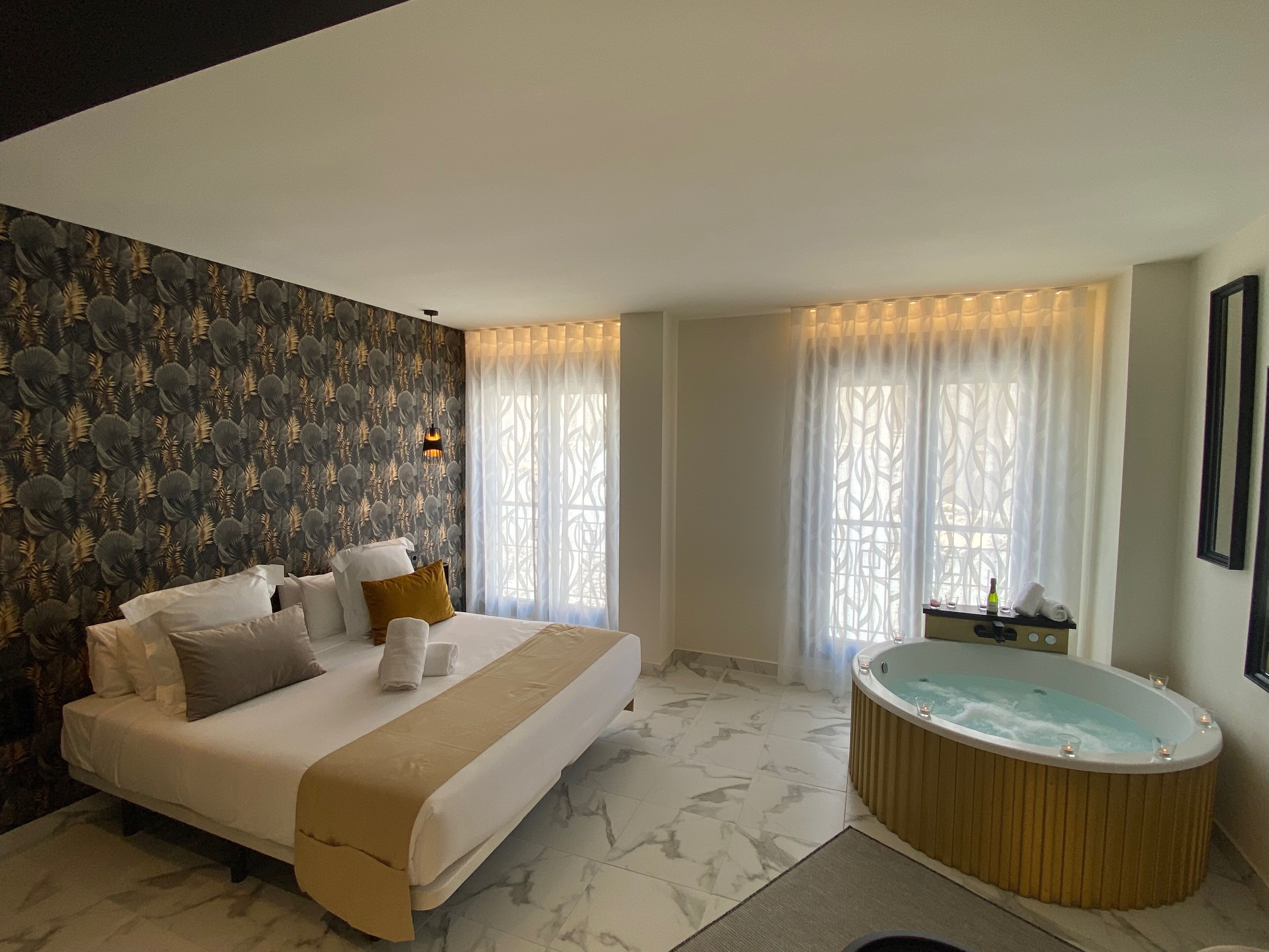 Una habitación de hotel moderna con una cama grande, una bañera y un papel tapiz estampado.