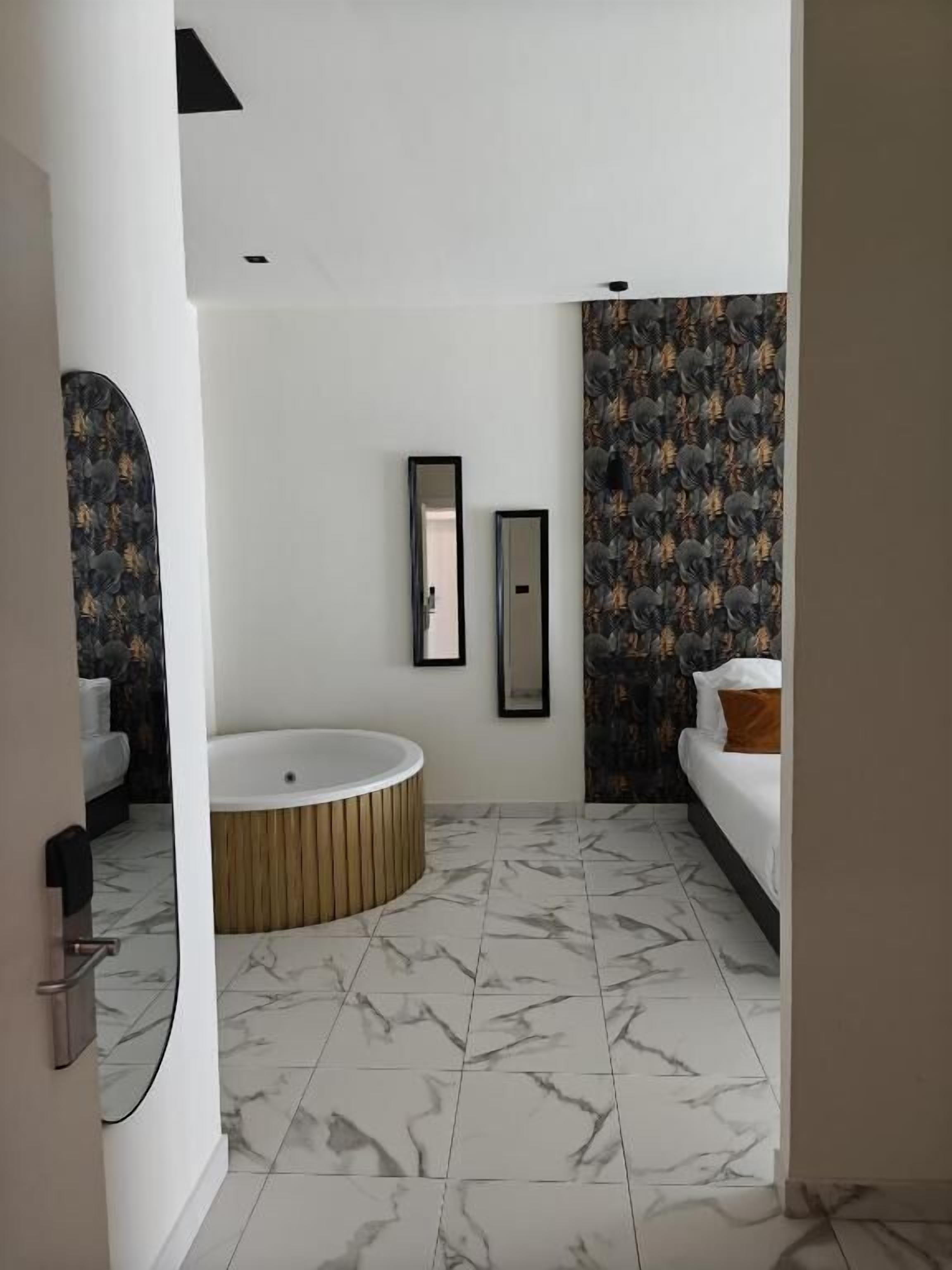 A modern bathroom with a freestanding bathtub, a large mirror, and a patterned wallpaper.