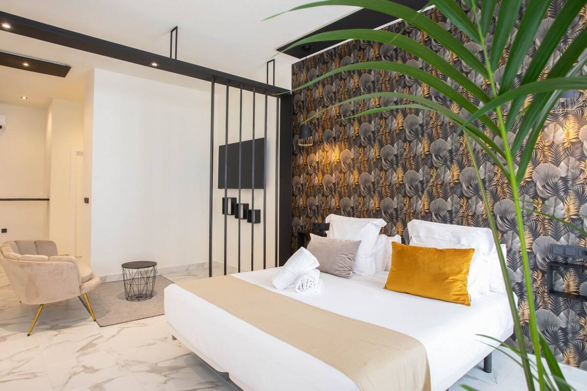 Un dormitorio moderno con una cama grande, una silla, una mesita redonda y una planta decorativa.