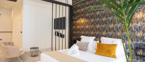 Un dormitorio moderno con una cama grande, una silla, una mesita redonda y una planta decorativa.