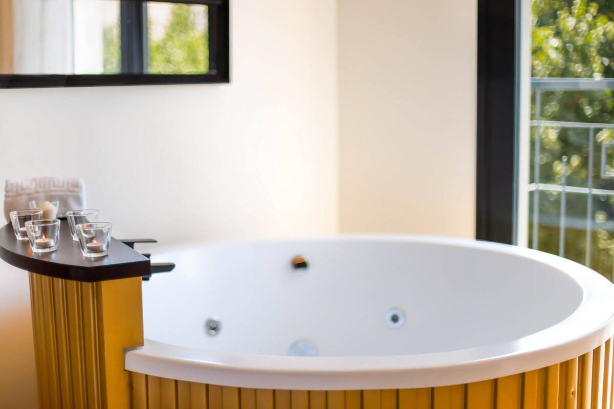 Un baño moderno con una bañera independiente, una mesita con velas y una ventana con vistas a la vegetación.