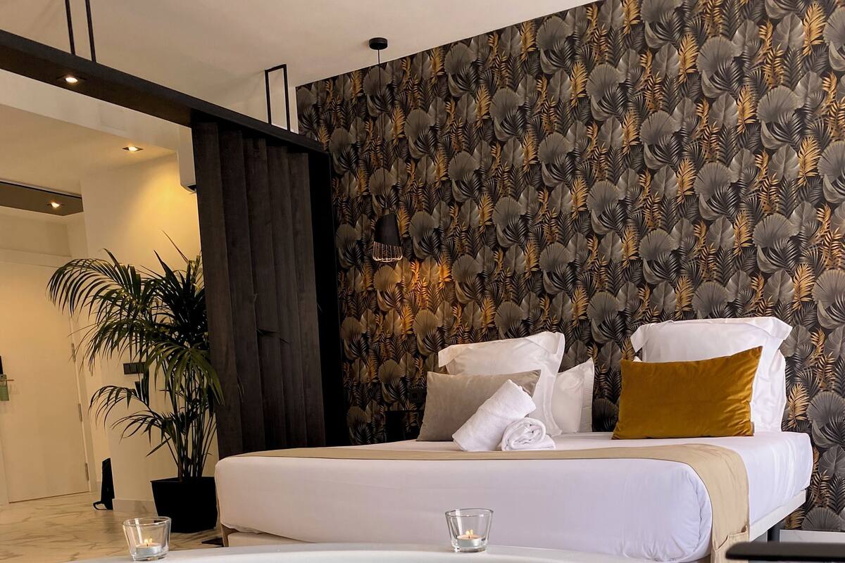 Una habitación de hotel moderna con una bañera grande, una cama bien hecha y una planta en maceta.