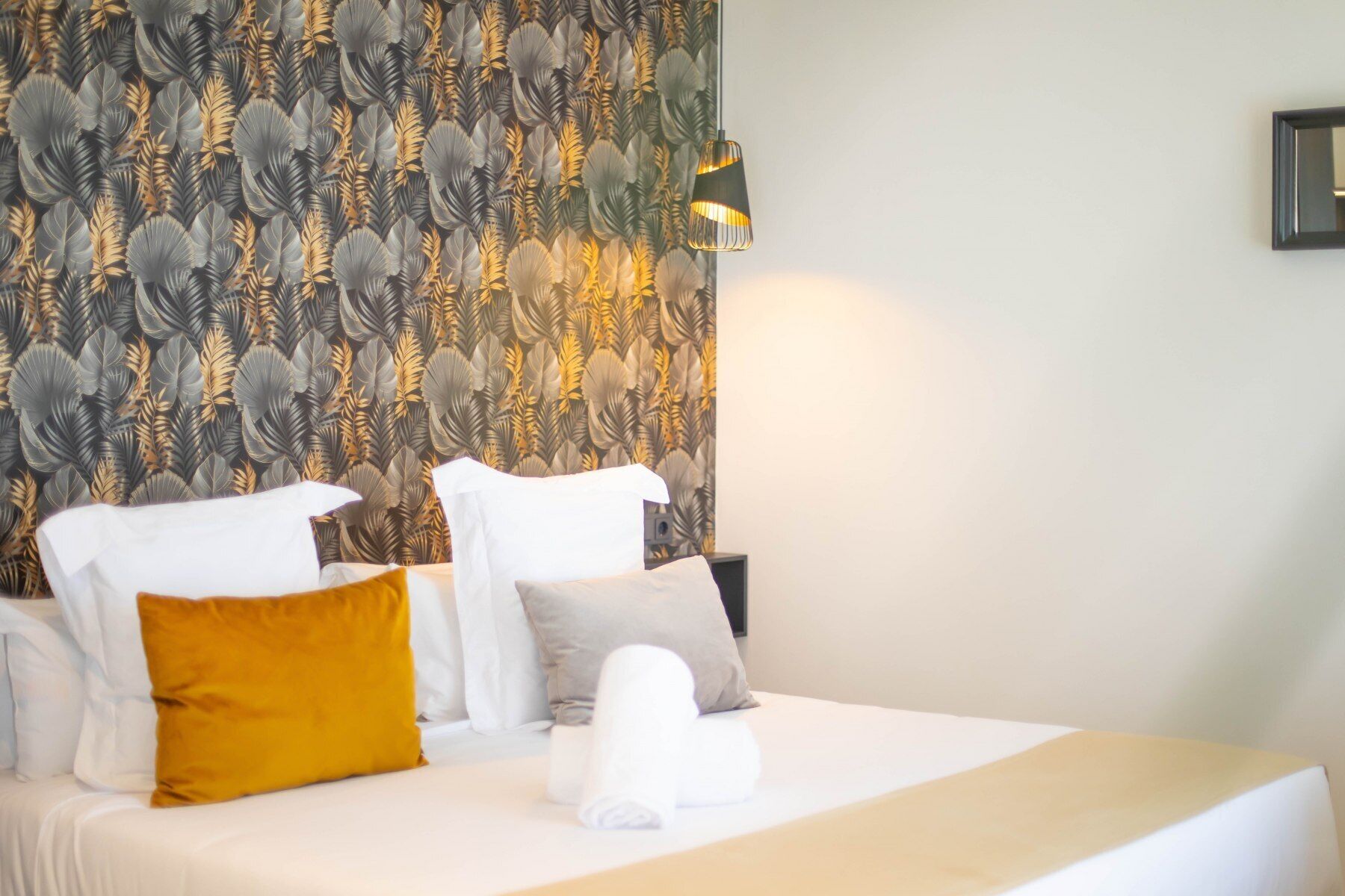 Una habitación de hotel con cama, almohadas, una pared con diseño de hojas y una lámpara colgante.