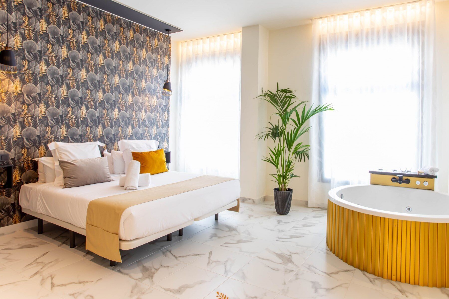 Una habitación de hotel moderna con una cama grande, una planta en maceta, una bañera y una ventana con cortinas.