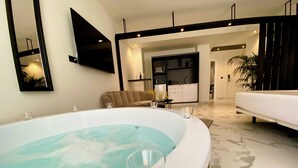 Un baño moderno con una bañera grande, un sofá, un comedor y una cocina al fondo.