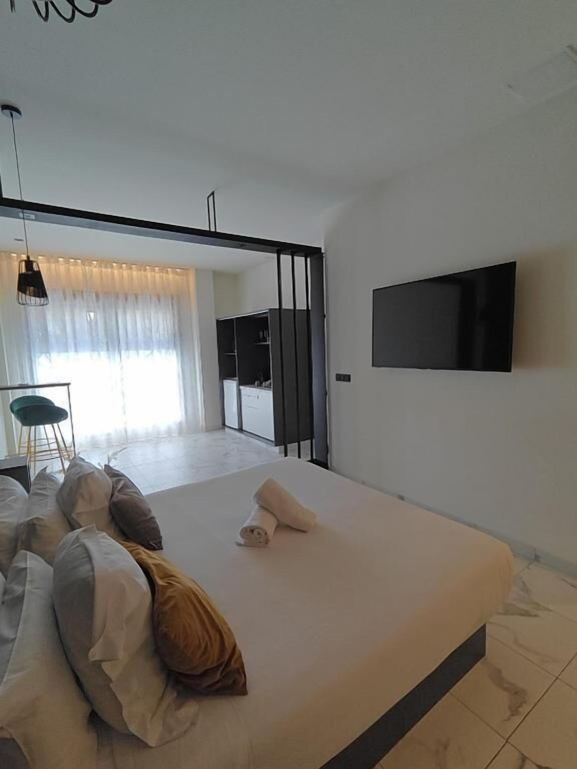 Ein modernes Schlafzimmer mit Bett, einem an der Wand montierten Fernseher und Blick in den Wohnbereich.