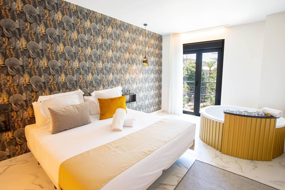 Habitación de hotel moderna con una cama grande, un pequeño rincón de descanso, una bañera y vistas al exterior.