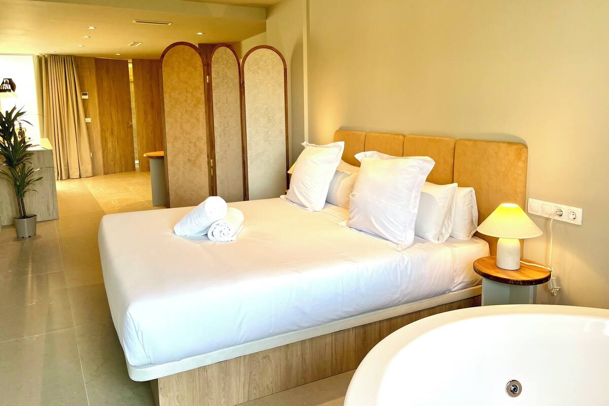 Une chambre d’hôtel avec un grand lit, une lampe de chevet, un lavabo rond blanc et une tête de lit en bois.