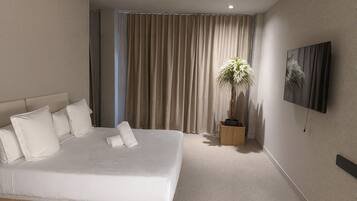 A modern hotel room with a large bed, a potted plant, a flat-screen TV, and a large window with curtains.